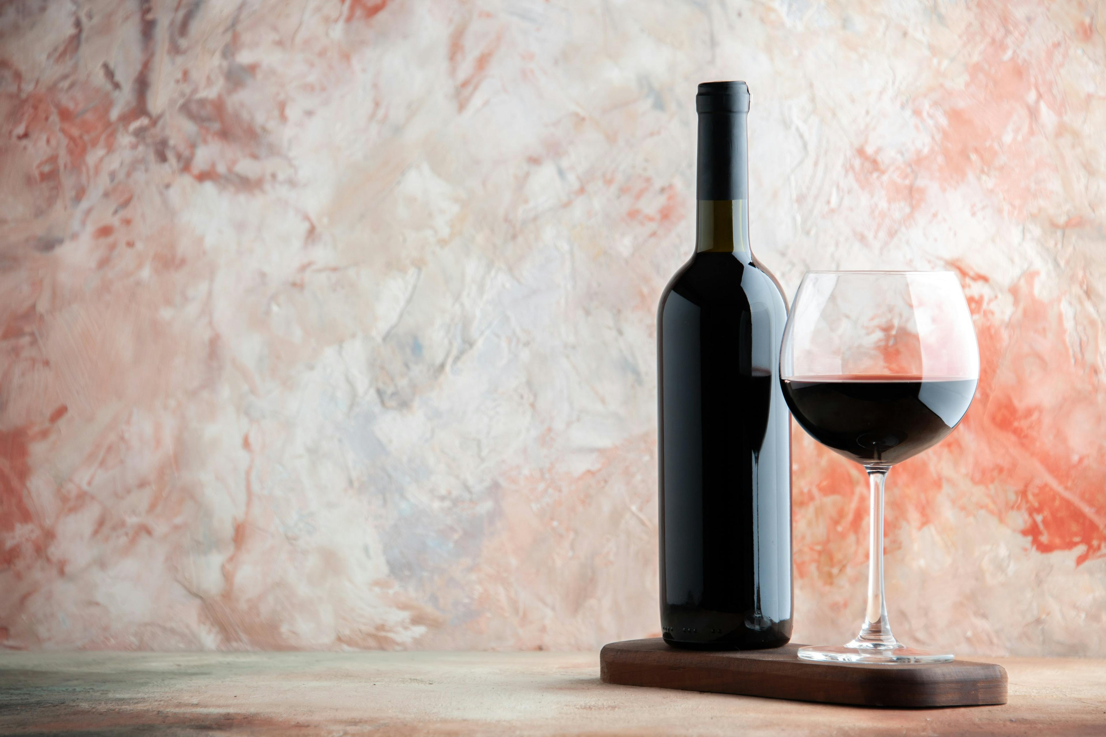 Elegant rödvinflaska och fyllt vinglas på träunderlägg med marmorbakgrund för vinälskare.