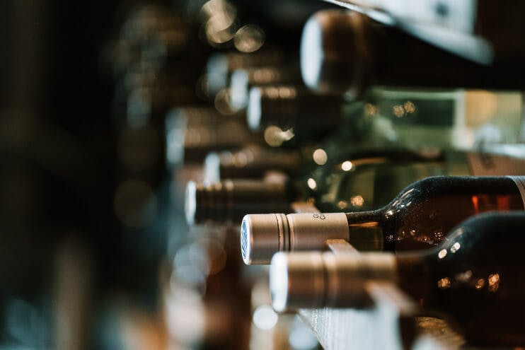 Horisontellt staplade vinflaskor med fokus på närmaste flaskans hals och kork, som en del av en omfattande vinprovning och recension.